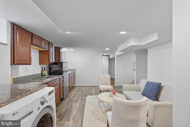 kitchen with backsplash, dark wood-type flooring, dark stone counters, appliances with stainless steel finishes, and washer / clothes dryer