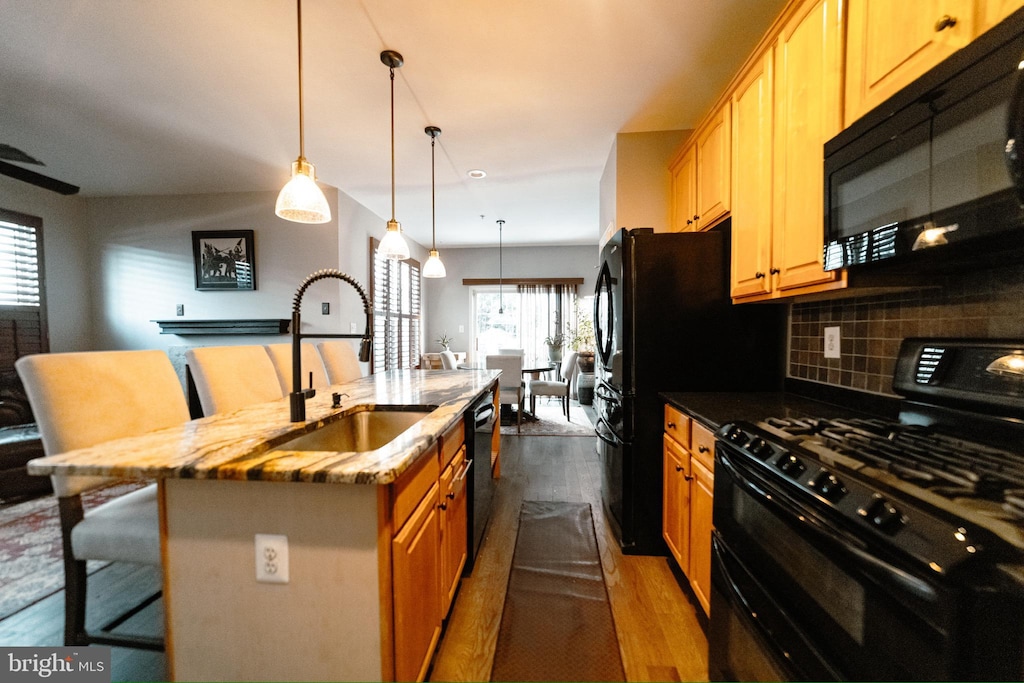 kitchen featuring backsplash, sink, black appliances, a breakfast bar area, and an island with sink