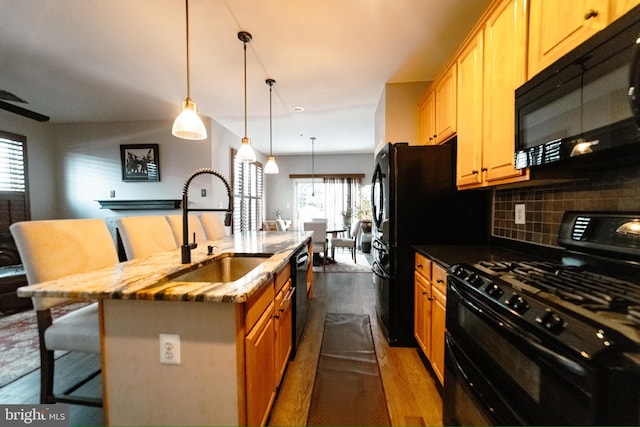 kitchen featuring backsplash, sink, black appliances, a breakfast bar area, and an island with sink