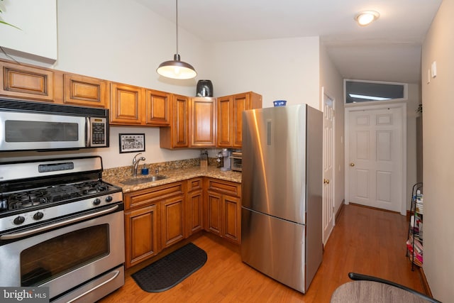 kitchen with sink, appliances with stainless steel finishes, decorative light fixtures, light hardwood / wood-style floors, and light stone counters