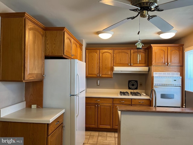 kitchen featuring white appliances, brown cabinetry, and under cabinet range hood