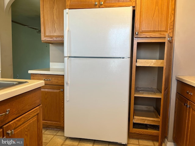 kitchen with brown cabinetry, arched walkways, light countertops, and freestanding refrigerator