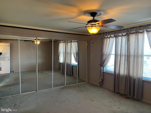 unfurnished bedroom with visible vents, multiple windows, carpet flooring, and ceiling fan