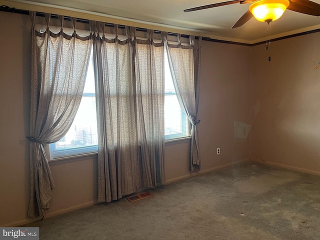 unfurnished room featuring a wealth of natural light, visible vents, ceiling fan, and carpet floors