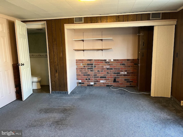 unfurnished bedroom with connected bathroom, visible vents, carpet floors, and wood walls