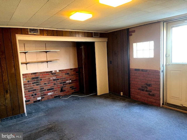 unfurnished room featuring carpet floors, wood walls, and brick wall