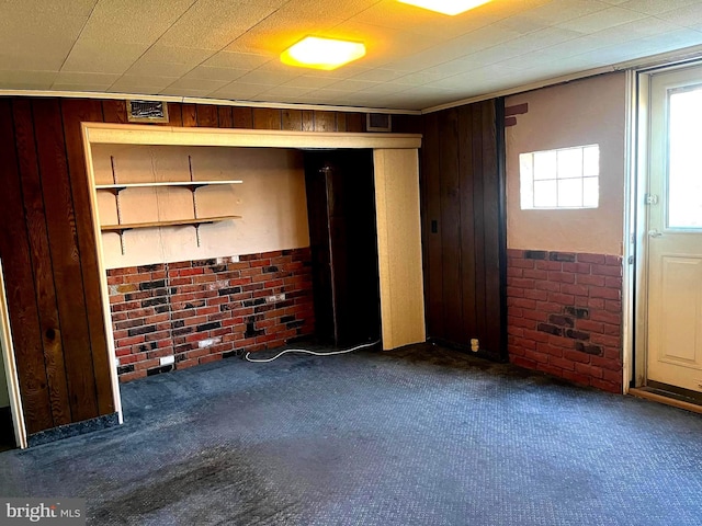 unfurnished room with carpet flooring, brick wall, and wooden walls