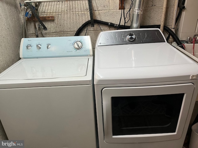 washroom featuring concrete block wall, separate washer and dryer, and laundry area