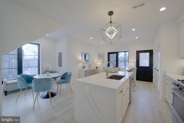 kitchen featuring sink, white cabinets, stainless steel stove, an island with sink, and hanging light fixtures