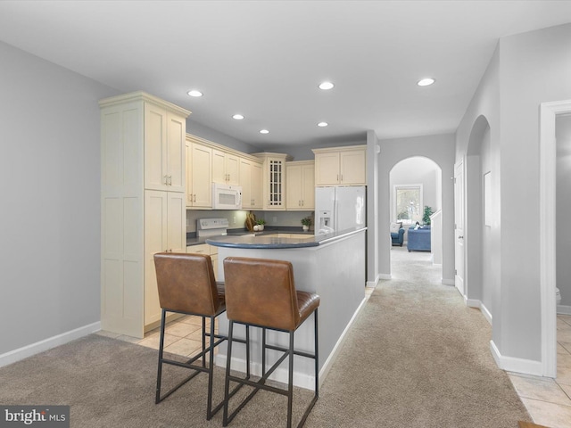 kitchen featuring a kitchen breakfast bar, light carpet, a center island, and white appliances