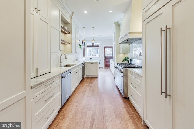 kitchen with high end appliances, custom range hood, white cabinetry, sink, and pendant lighting