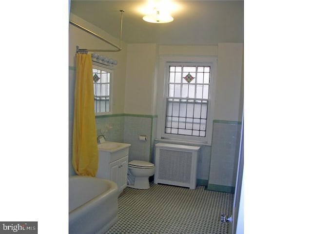 bathroom with radiator, a healthy amount of sunlight, tile walls, and toilet