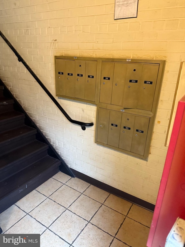 stairs with tile patterned flooring, a mail area, and brick wall