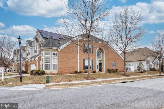 view of front of property with a garage, concrete driveway, solar panels, a residential view, and brick siding