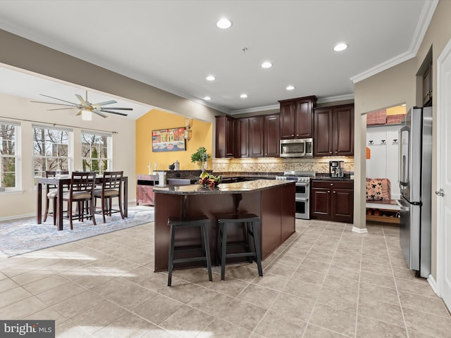 kitchen featuring dark brown cabinetry, decorative backsplash, appliances with stainless steel finishes, a kitchen breakfast bar, and crown molding