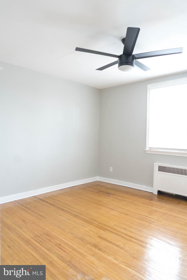 empty room featuring ceiling fan, radiator heating unit, and light hardwood / wood-style flooring