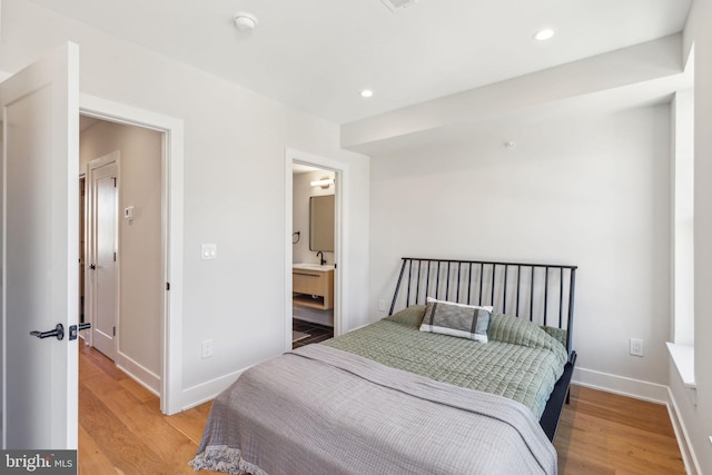 bedroom featuring light hardwood / wood-style flooring, ensuite bath, and sink