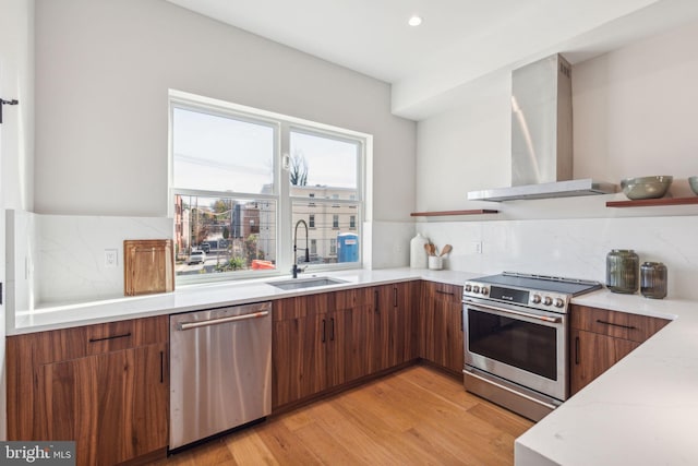 kitchen featuring backsplash, sink, wall chimney exhaust hood, appliances with stainless steel finishes, and light hardwood / wood-style floors