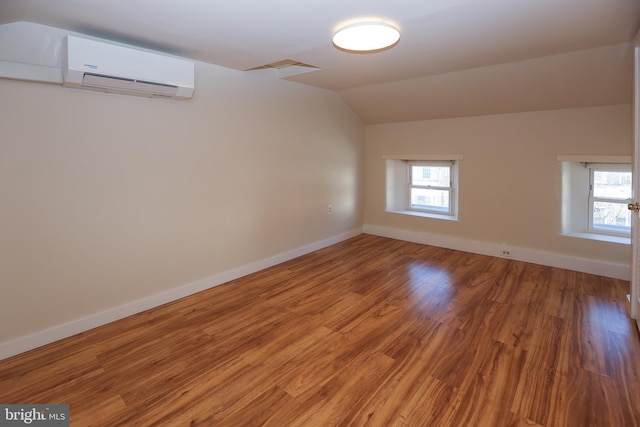 unfurnished room featuring vaulted ceiling, wood-type flooring, and a wall mounted air conditioner