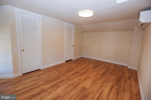 interior space with light wood-type flooring, lofted ceiling, and a wall unit AC