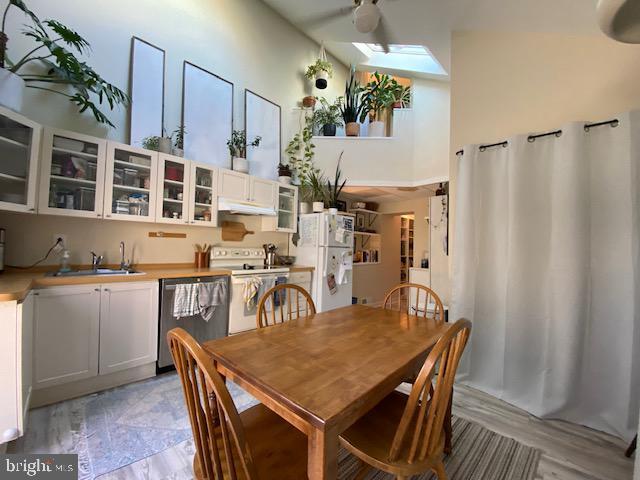 dining area with a skylight, light hardwood / wood-style flooring, a high ceiling, and sink