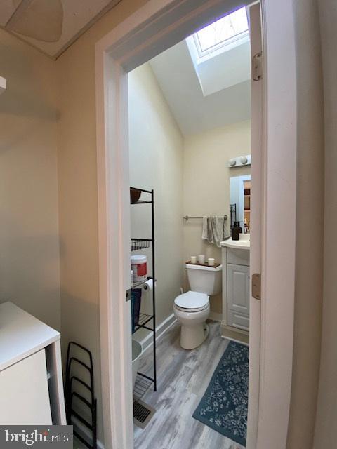 bathroom featuring hardwood / wood-style floors, vanity, toilet, and lofted ceiling with skylight