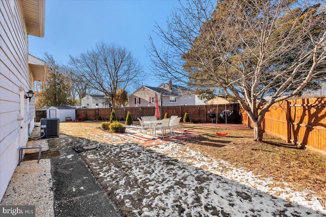 yard layered in snow with a patio area, central air condition unit, and a storage shed