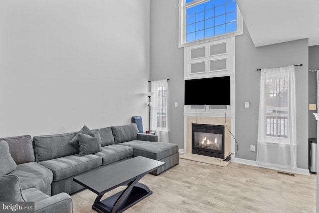 living room with a towering ceiling, light hardwood / wood-style flooring, and a tiled fireplace