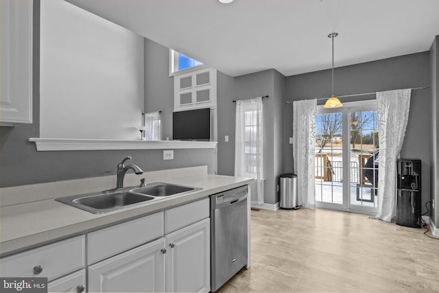 kitchen with sink, light hardwood / wood-style flooring, stainless steel dishwasher, decorative light fixtures, and white cabinets