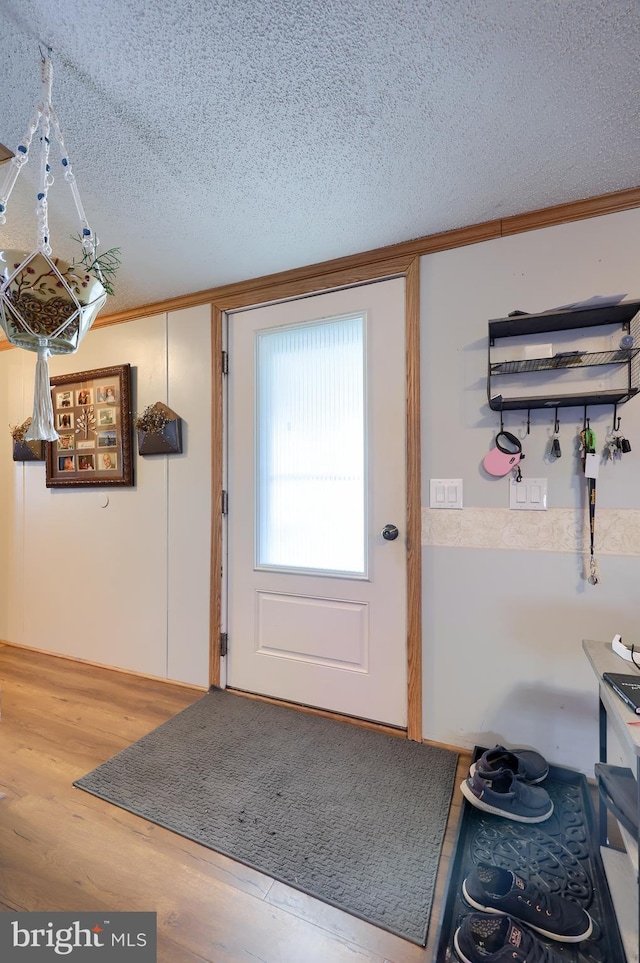 doorway to outside featuring ornamental molding, wood-type flooring, and a textured ceiling