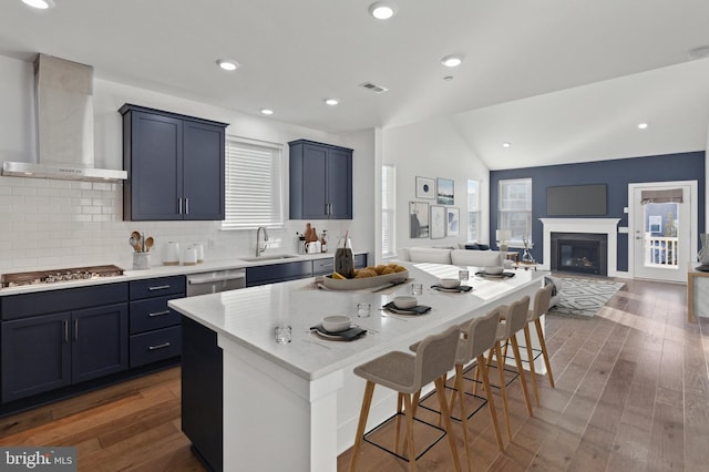 kitchen with sink, wall chimney exhaust hood, vaulted ceiling, a kitchen bar, and appliances with stainless steel finishes