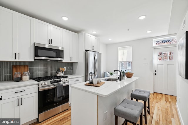 kitchen with a kitchen bar, stainless steel appliances, sink, white cabinetry, and an island with sink