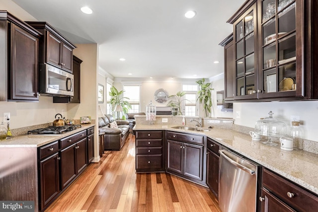 kitchen with ornamental molding, dark brown cabinetry, stainless steel appliances, sink, and light hardwood / wood-style floors