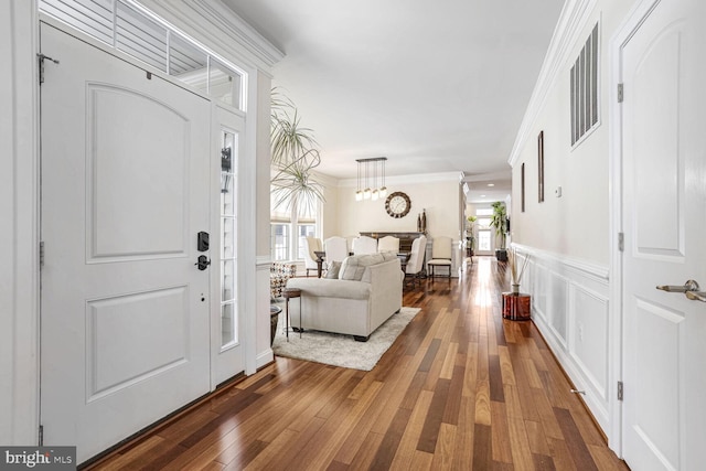 foyer entrance featuring ornamental molding, dark wood-type flooring, and an inviting chandelier