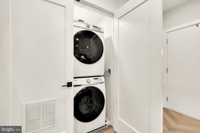 laundry area with light parquet floors and stacked washing maching and dryer