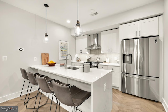 kitchen featuring light parquet flooring, appliances with stainless steel finishes, wall chimney range hood, and white cabinets