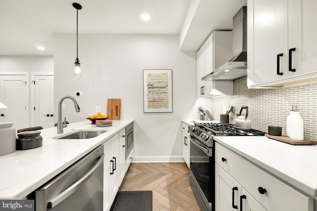 kitchen with pendant lighting, sink, wall chimney range hood, appliances with stainless steel finishes, and light parquet flooring