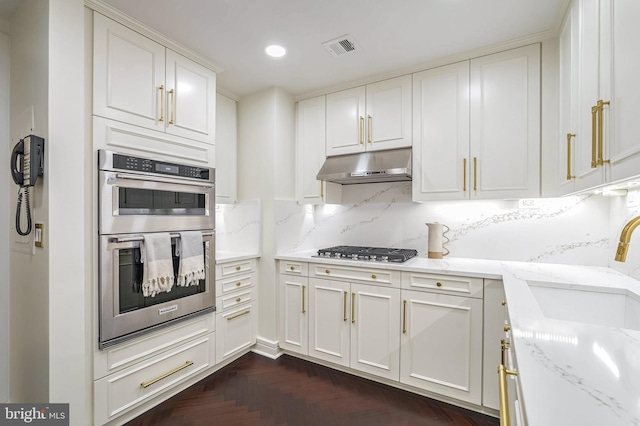 kitchen with decorative backsplash, dark parquet flooring, light stone counters, stainless steel appliances, and white cabinets