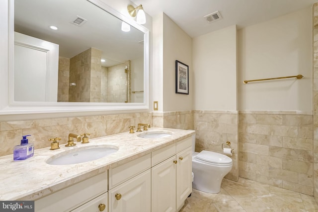 bathroom featuring vanity, tile patterned floors, toilet, tile walls, and a tile shower