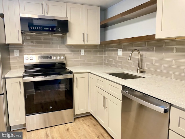 kitchen featuring decorative backsplash, appliances with stainless steel finishes, light stone counters, sink, and light hardwood / wood-style floors