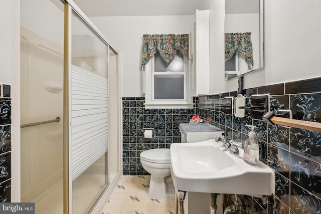 bathroom featuring sink, a shower with door, tile walls, and toilet