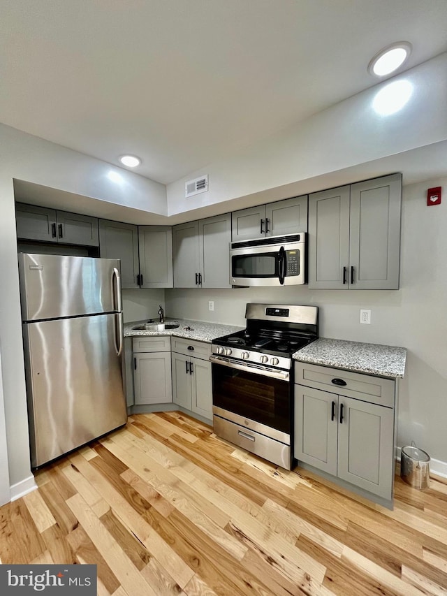 kitchen with gray cabinets, light hardwood / wood-style flooring, stainless steel appliances, and sink