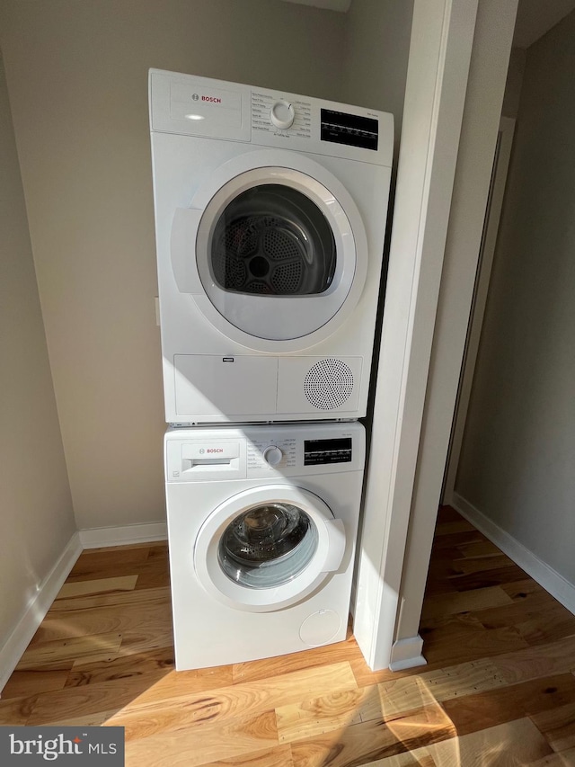 laundry area with hardwood / wood-style flooring and stacked washer and clothes dryer