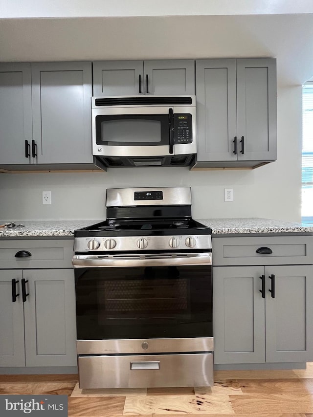 kitchen featuring gray cabinets, light stone countertops, stainless steel appliances, and light hardwood / wood-style floors