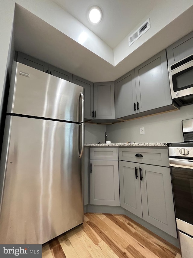 kitchen featuring gray cabinets, stainless steel appliances, light hardwood / wood-style flooring, and light stone counters