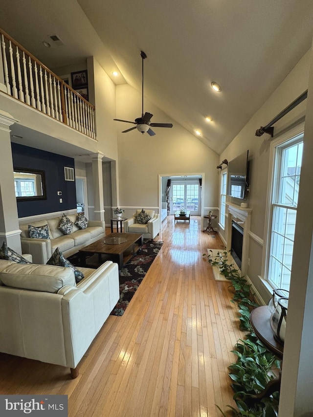 living room featuring ceiling fan, light hardwood / wood-style floors, ornate columns, and high vaulted ceiling