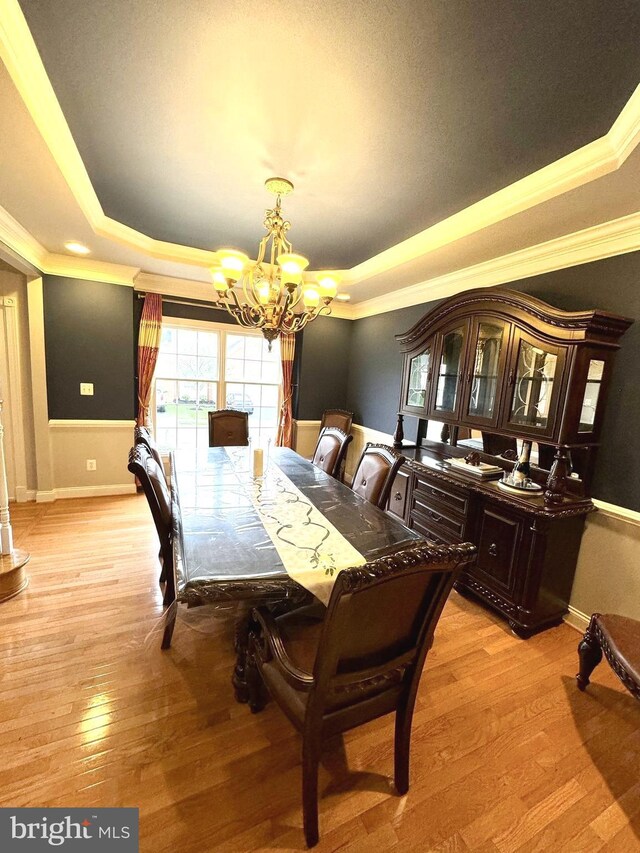 dining area featuring a notable chandelier, light hardwood / wood-style floors, and a raised ceiling