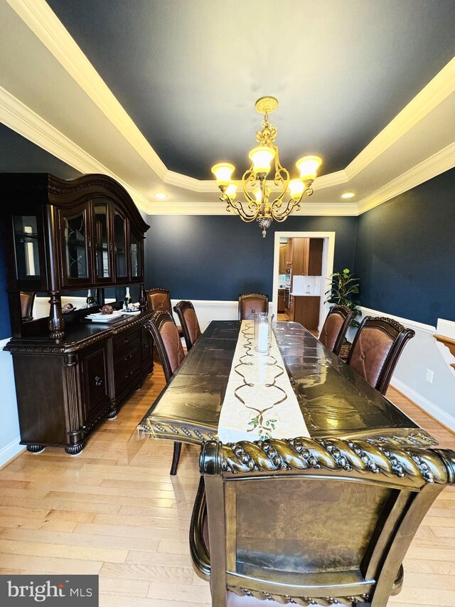 dining area with ornamental molding, light wood-type flooring, a raised ceiling, and a notable chandelier