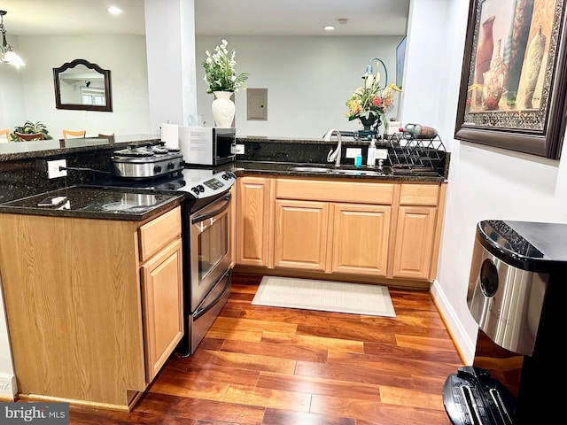 kitchen with sink, dark stone countertops, appliances with stainless steel finishes, decorative light fixtures, and dark hardwood / wood-style flooring