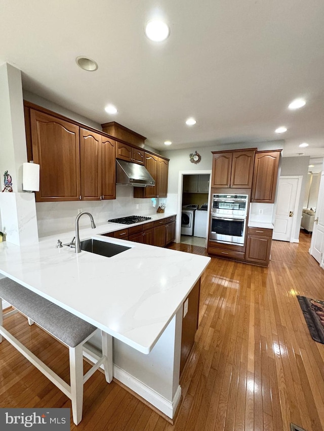 kitchen featuring kitchen peninsula, a kitchen breakfast bar, stainless steel appliances, sink, and washing machine and clothes dryer